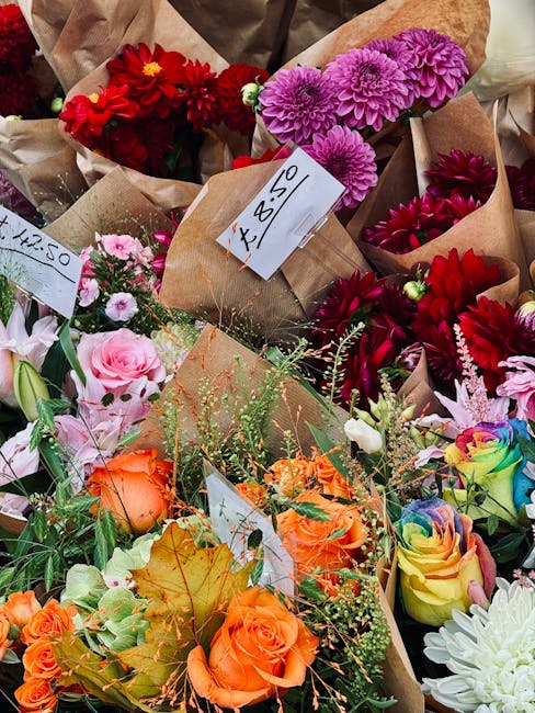 A vibrant assortment of freshly cut flowers arranged in bouquets, featuring red, pink, purple, orange, and rainbow-colored roses, dahlias, chrysanthemums, and other blooms. The flowers are wrapped in